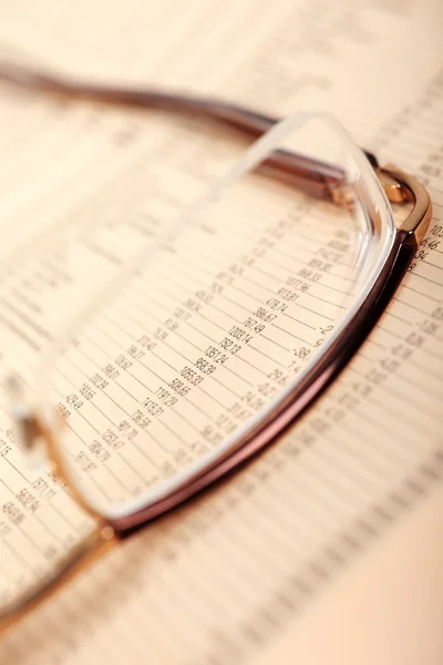 Macro of financial data through eyeglasses, laying on newspaper. — Stock Photo, Image