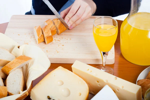 Стол с едой и женские руки режут хлеб — стоковое фото