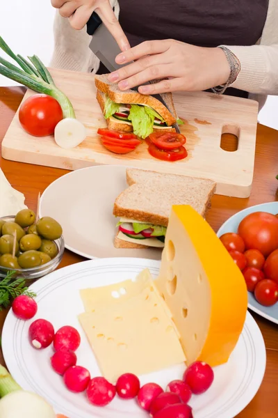 Tabel met eten en vrouw halveren van sandwich — Stockfoto