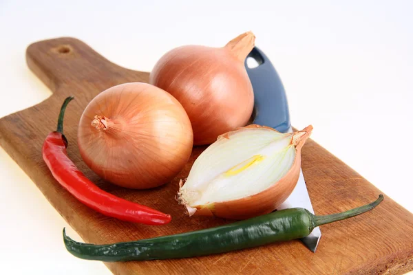 Cebolas, pimentas e uma faca em uma tábua de corte — Fotografia de Stock