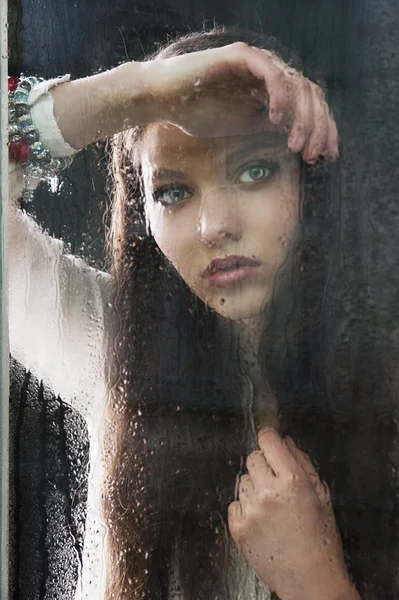 Die denkende Frau am Fenster mit der Hand nahe der Brust — Stockfoto
