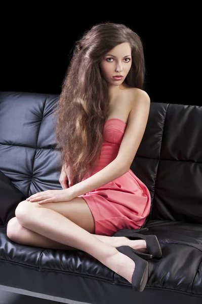 Brunette in pink on sofa, she has right hand on the right leg — Stock Photo, Image