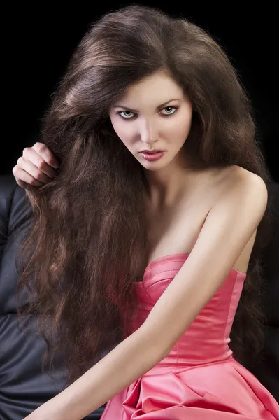 Brünett in rosa auf dem Sofa, sie hält eine Haarsträhne mit rechten Haaren — Stockfoto