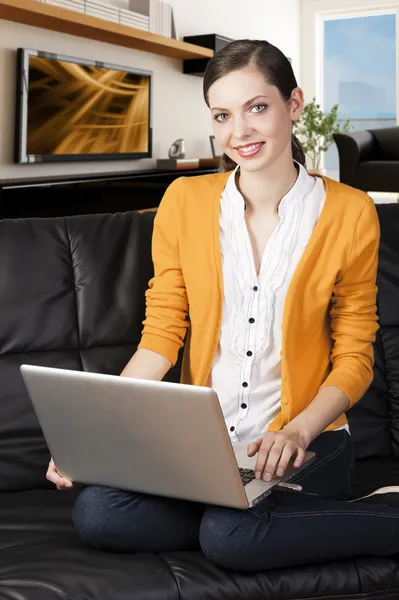 Menina no sofá com laptop, ela sorri e olha para a lente — Fotografia de Stock