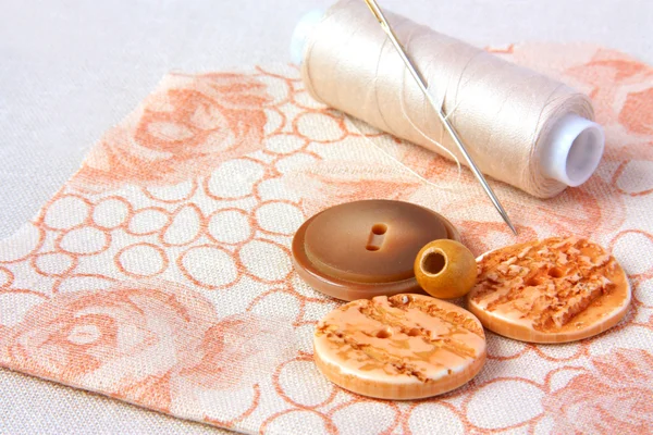 Carrete beige de hilo y botones sobre un tejido floral —  Fotos de Stock