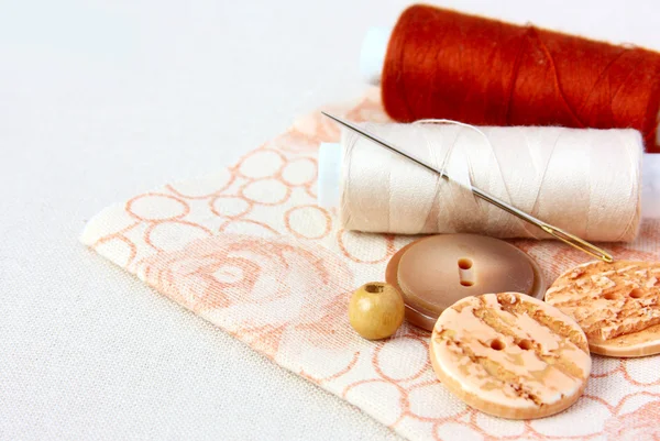 Beige spoel van draad en knoppen op een floral stof — Stockfoto