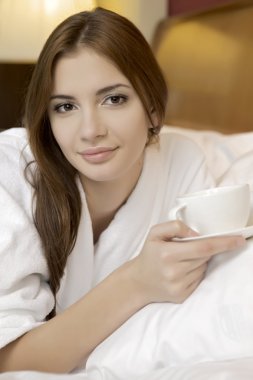 Portrait of beautiful woman with cup on bed clipart