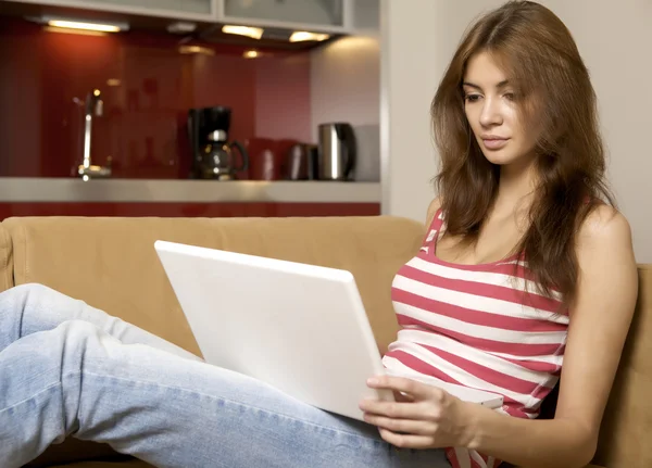 Giovane donna sdraiata su un divano bianco con un computer portatile . — Foto Stock