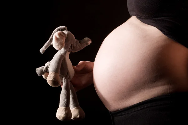 Femme enceinte ventre avec jouet sur noir — Photo
