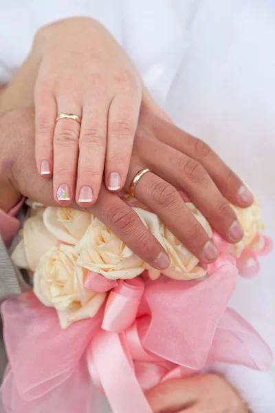 Les mains du marié et de la mariée avec des alliances sur un bouquet de mariage — Photo