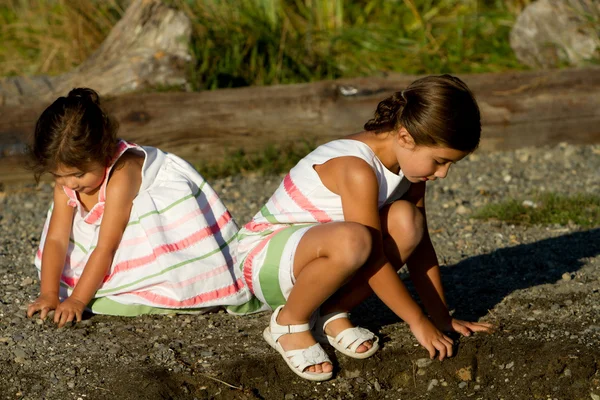Sisters crouch to play with sand & rocks. — Stock Photo, Image
