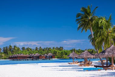 Palm trees over sandy tropical beach with villas over water clipart