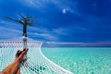 Man's legs in hammock over tropical lagoon clipart