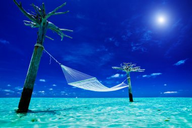 Empty over-water hammock in the middle of tropical lagoon clipart