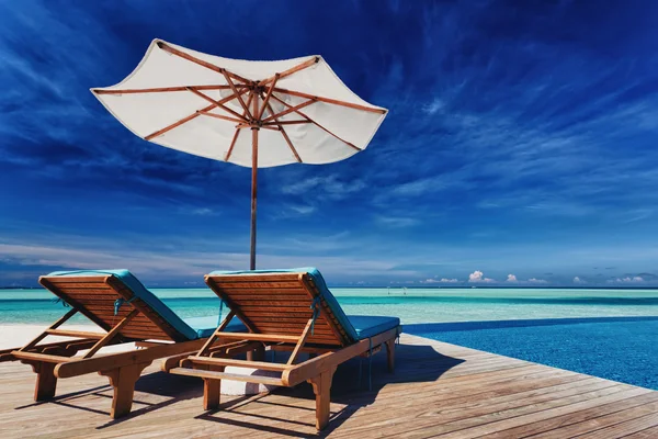 Ligstoelen en zwembad met overstroomrand over tropische lagune — Stockfoto
