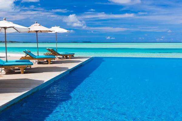 Liegestühle und Infinity-Pool über tropischer Lagune — Stockfoto