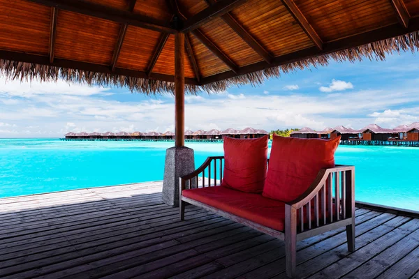 Sofa z czerwone poduszki na molo w tropikalną laguną — Zdjęcie stockowe