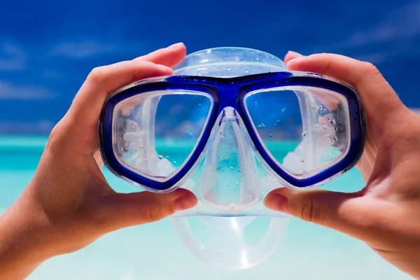 Mão segurando snorkel googles contra praia — Fotografia de Stock