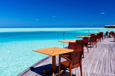 Tables and chairs at tropical beach restaurant clipart