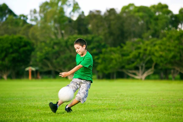 Aufgeregter Junge kickt Ball ins Gras — Stockfoto