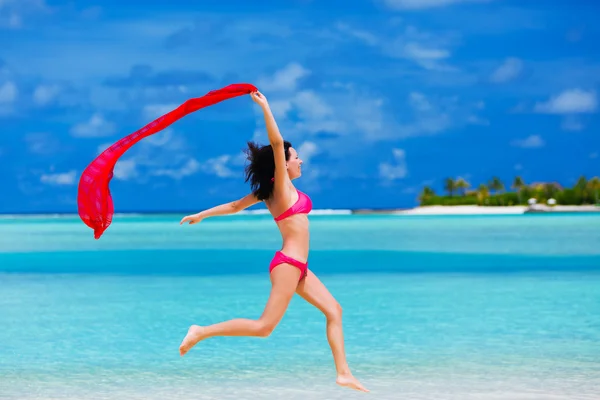 年轻女子和一条红色的围巾在沙滩上跳跃 — 图库照片
