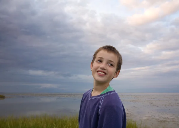 Drôle litle garçon souriant largement, mer du soir du nord dans le dos — Photo
