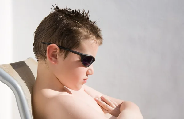 Cute little boy in dark shades suntanning, whitewashed wall in the backgrou — Stock Photo, Image