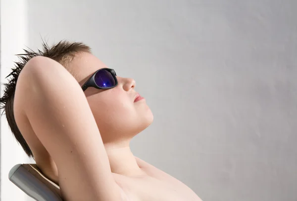 Cute little boy in dark shades suntanning, whitewashed wall in t — Stock Photo, Image