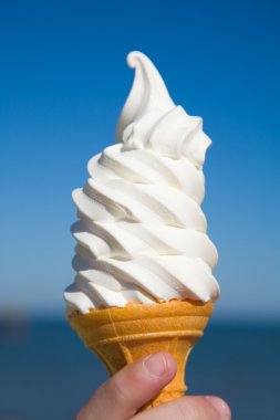 Large portion of soft ice-cream in child's hand, sea and blue sky in the background clipart