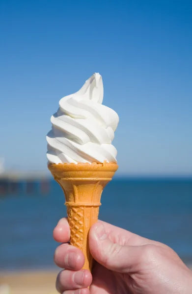 Большая часть мягкого мороженого в руке человека, море и голубое небо на заднем плане — стоковое фото