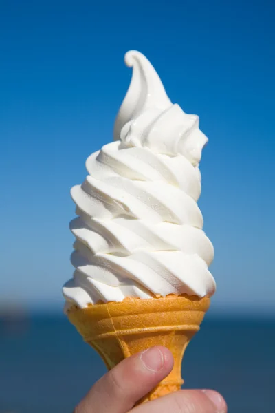 Большая часть мягкого мороженого в руке ребенка, море и голубое небо на заднем плане — стоковое фото
