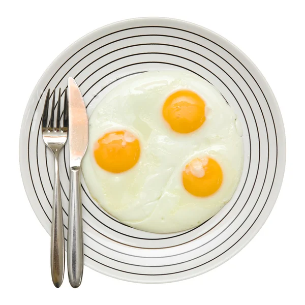 stock image Three fried unbroken eggs on white plate with black stipe; fork and knife on the left, shot from the top; isolated;