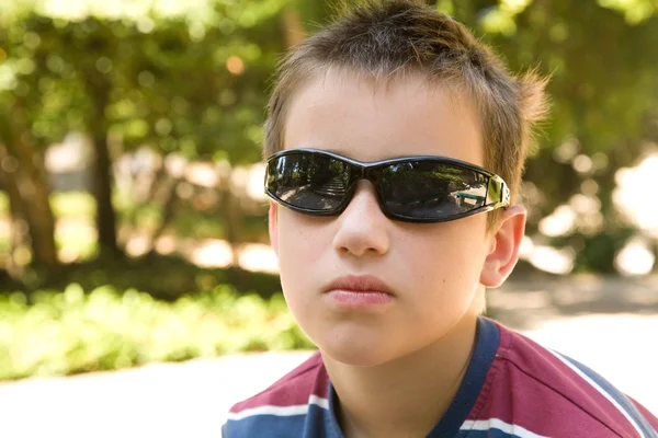Little caucasian boy in dark shades in sunny park — Stock Photo, Image