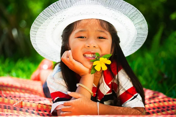 Jong meisje liggend op een weide met een hoed op haar hoofd en een bloem — Stockfoto