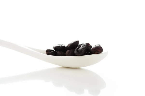 Kaffeebohnen in einem weißen Löffel auf weißem Hintergrund mit hellem Ref — Stockfoto