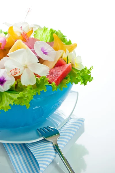 Fruitsalade met eetbare bloemen in een blauwe kom uit ijs op wit — Stockfoto