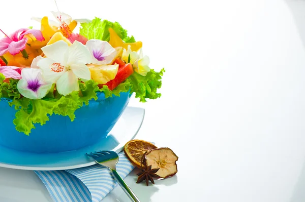 Fruit salad with edible flowers in a blue bowl from ice on white — Stock Photo, Image
