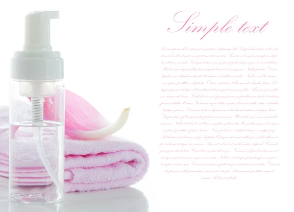 Een roze handdoeken met een lotus petal en een fles van cosmetische op whi — Stockfoto