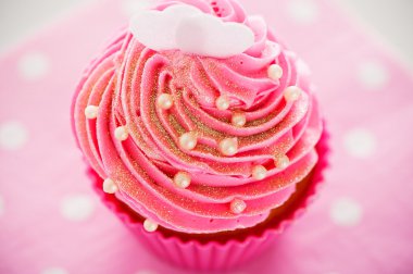 A cupcake in a pink baking cups with pink cream, white decoratio clipart