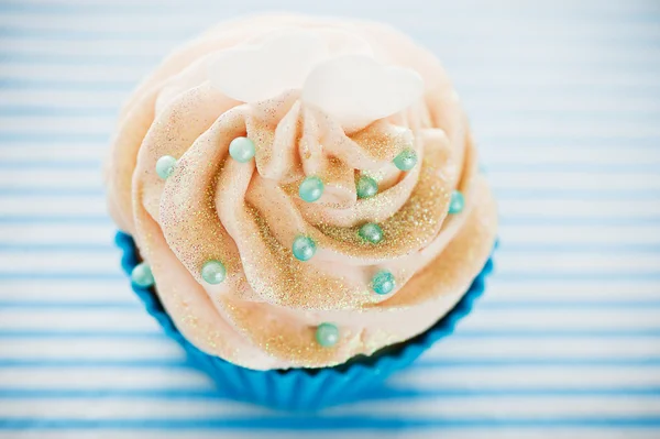 A cupcake in a blue baking cups with white cream, blue decoratio — Stock Photo, Image