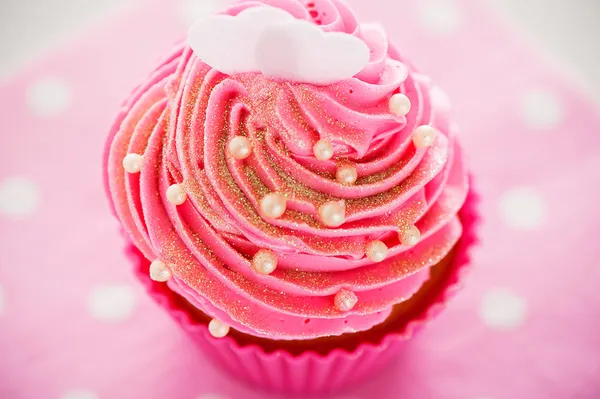 Um cupcake em uma xícara de cozimento rosa com creme rosa, decoro branco — Fotografia de Stock