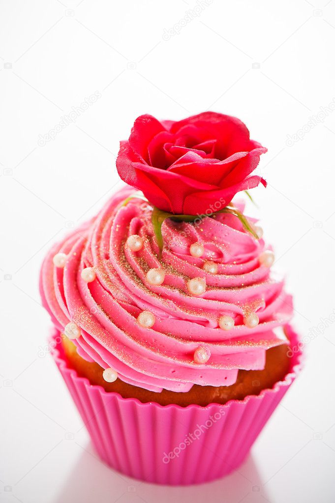 A cupcake in a pink baking cups with pink cream, white decoratio
