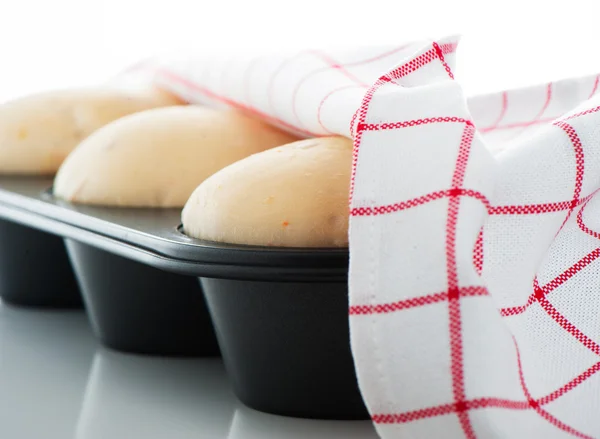 Massa de farinha de levedura em uma panela de muffin com uma toalha branca e vermelha no branco — Fotografia de Stock