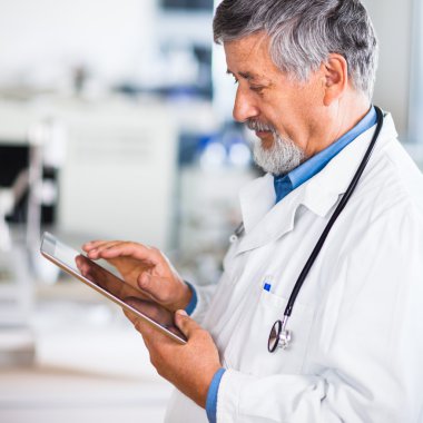 Senior doctor using his tablet computer at work clipart