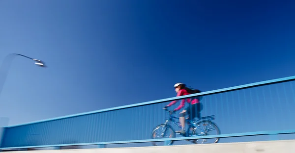 Female cyclist going over a bridge on a lovely sunny day — Stock Photo, Image