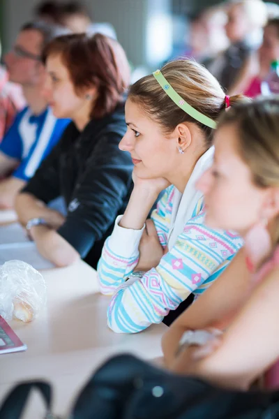 Fiatal, csinos női főiskolai hallgató ül egy osztályteremben — Stock Fotó
