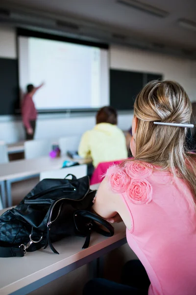 Ung, ganska kvinnlig collegestudent som sitter i ett klassrum — Stockfoto