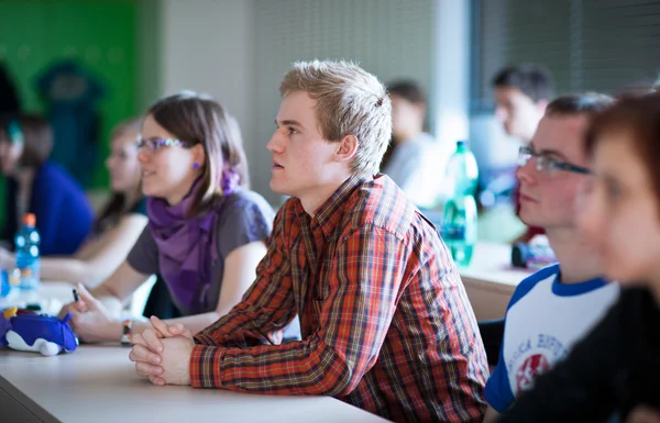 Ung, stilig collegestudent sitter i ett klassrum — Stockfoto