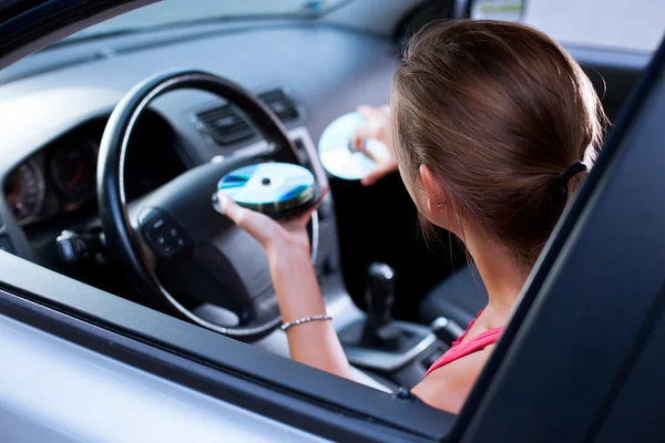 Jovem motorista do sexo feminino tocando música no carro (mudando CDs ) — Fotografia de Stock
