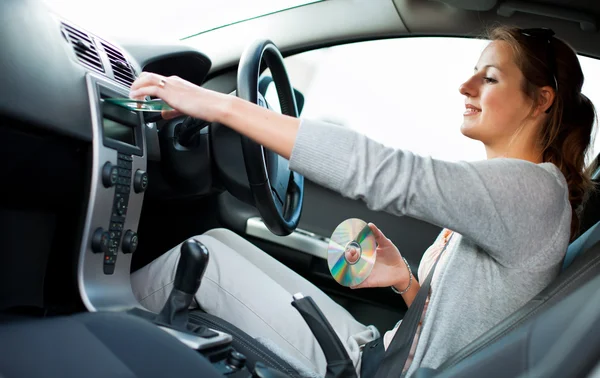 Jovem motorista do sexo feminino tocando música no carro (mudando CDs ) — Fotografia de Stock